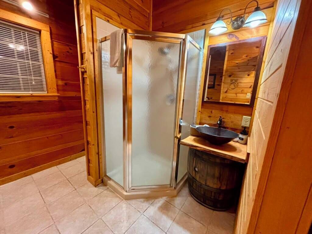 Interior de una cabaña de madera con cabina de ducha de vidrio, un lavabo y un barril de madera.