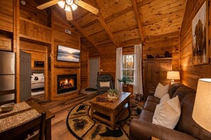 Ein gemütliches Blockhaus-Interieur mit Kamin, Fernseher, Sofa und Essbereich.