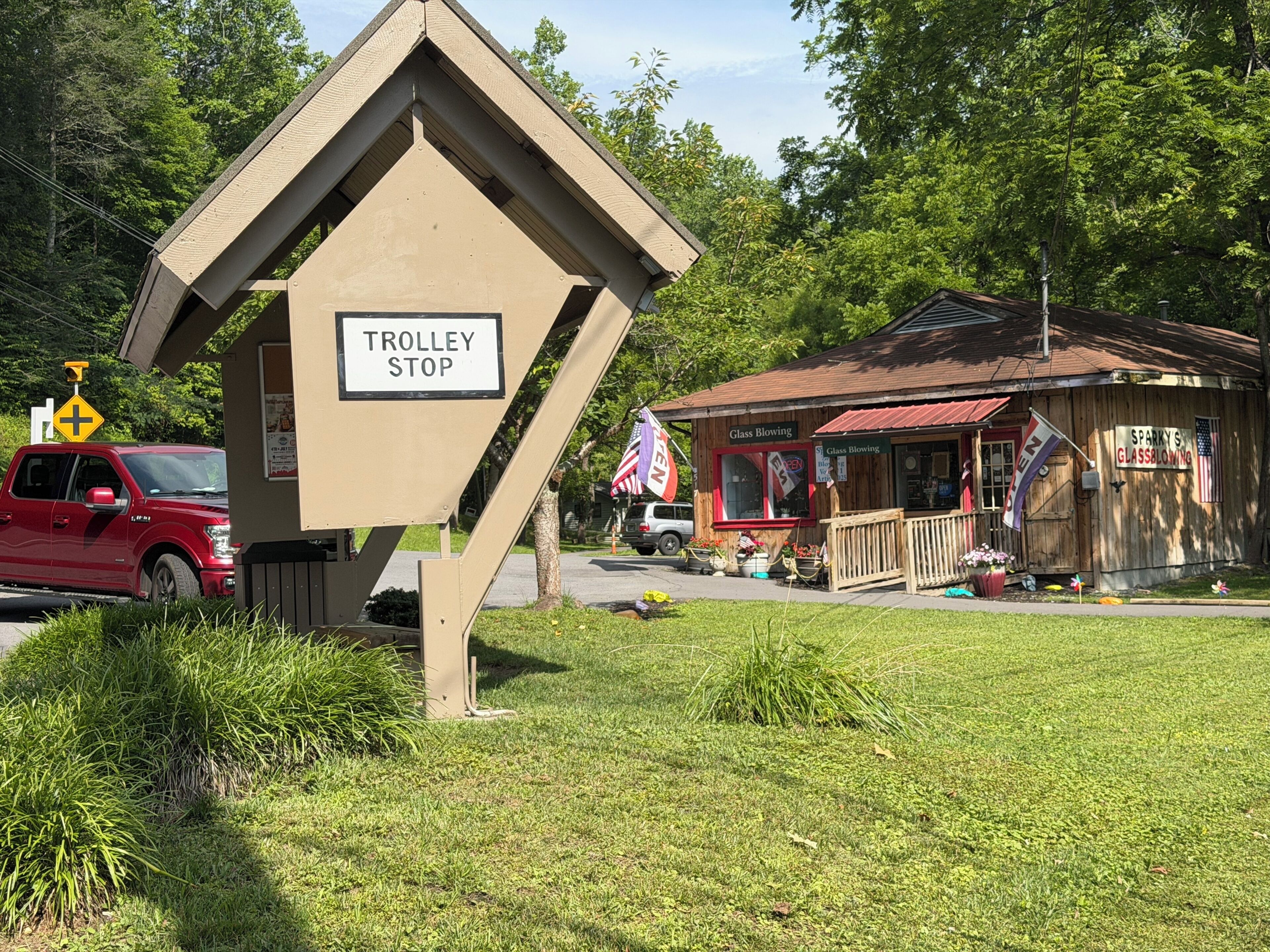 A trolley stop sign, a red vehicle, and a small wooden building with an American flag.