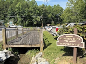 A wooden deck leading to a parking area with a sign indicating the entrance to Morning Mist Village. - Sleeps 4, Couples Cabin, Hot Tub, Fireplace, Pet Friendly, 8.8 Mi to Gatlinburg (Gatlinburg)