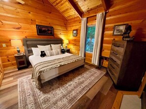 A wooden-paneled bedroom with a bed, nightstands, a dresser, and a window with curtains. - Sleeps 4, Couples Cabin, Hot Tub, Fireplace, Pet Friendly, 8.8 Mi to Gatlinburg (Gatlinburg)