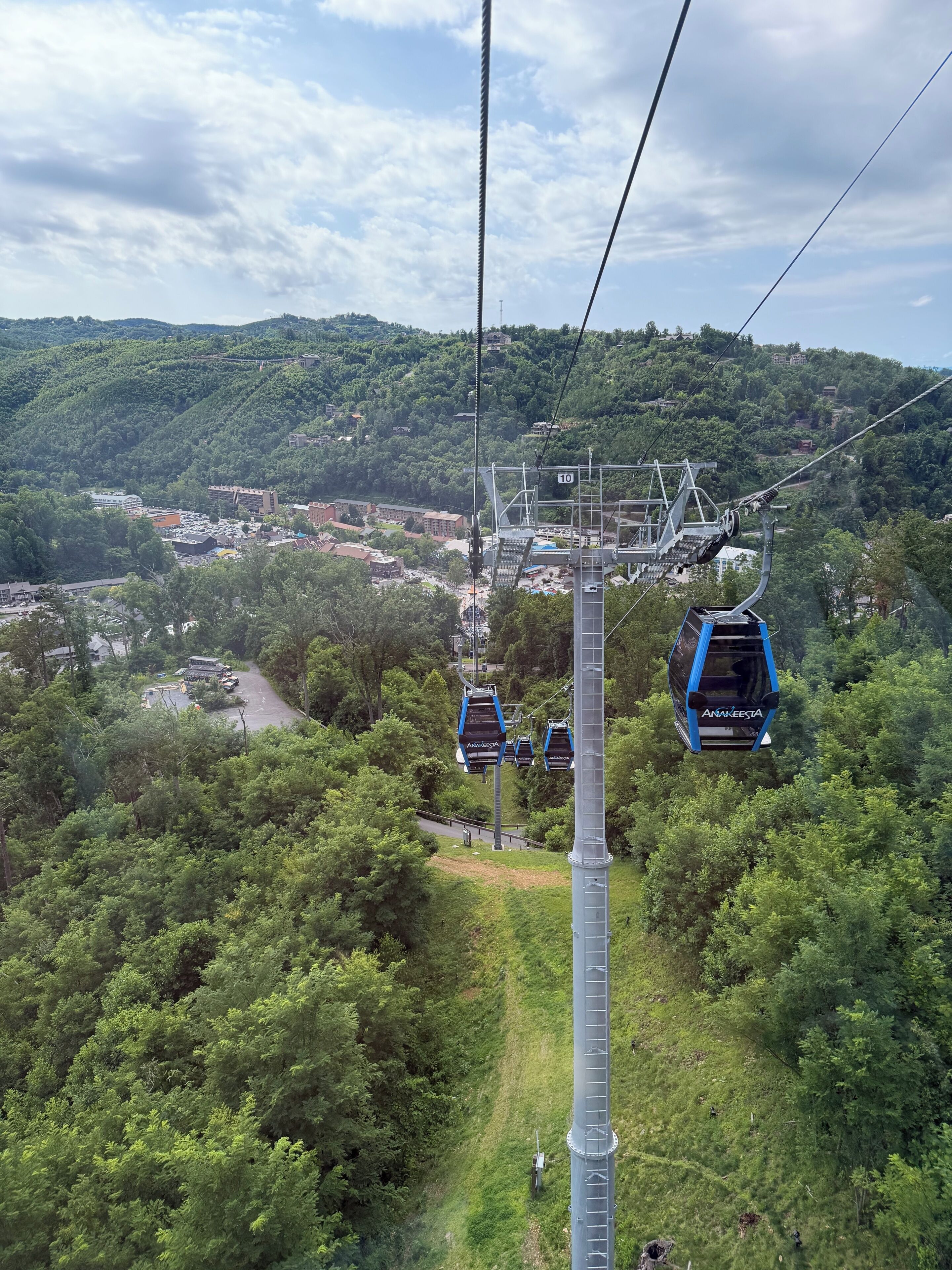 Sistema de teleférico con cabinas identificadas como 'Anakeesta' en una zona montañosa con abundante vegetación y un pueblo pequeño en la parte inferior.
