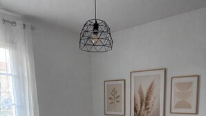 Ett sovrum med en säng, en geometrisk hänglampa och inramade botaniska tryck på väggen.