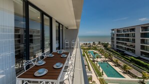Ein Balkon mit einem Holztisch und -stühlen, der auf einen Pool und ein Gebäude mit mehreren Balkonen blickt.