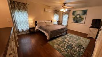 Un dormitorio con cama, ventilador de techo, televisor y un cuadro en la pared.