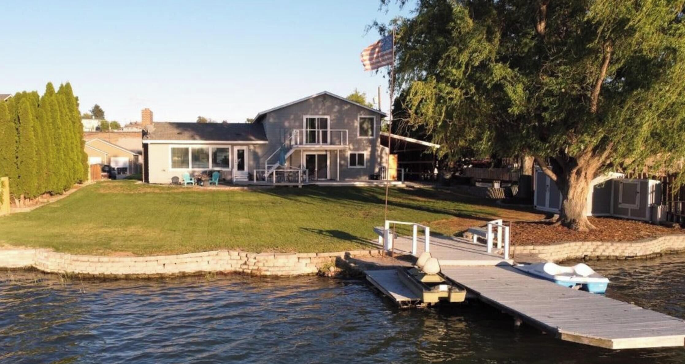 A house with a dock extending into a body of water, a flagpole with an American flag, and a well-maintained lawn.