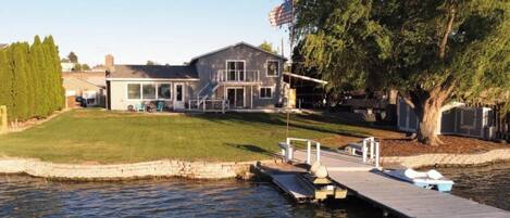 A house with a dock extending into a body of water, a flagpole with an American flag, and a well-maintained lawn.