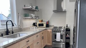 A modern kitchen with a stainless steel refrigerator, a built-in oven, and a microwave. There are wooden cabinets with black handles and a granite countertop. - Lovely studio in charming Arcata perfect for your stay (Arcata)