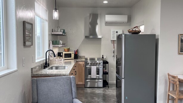 A modern kitchen with a grey sofa, a round ottoman, and a dining area with a wooden chair. - Lovely studio in charming Arcata perfect for your stay (Arcata)