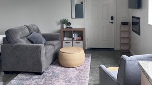 A modern living room with a grey sofa, ottoman, and armchair, a small bookshelf, a mirror, and a TV mounted on the wall. - Lovely studio in charming Arcata perfect for your stay (Arcata)