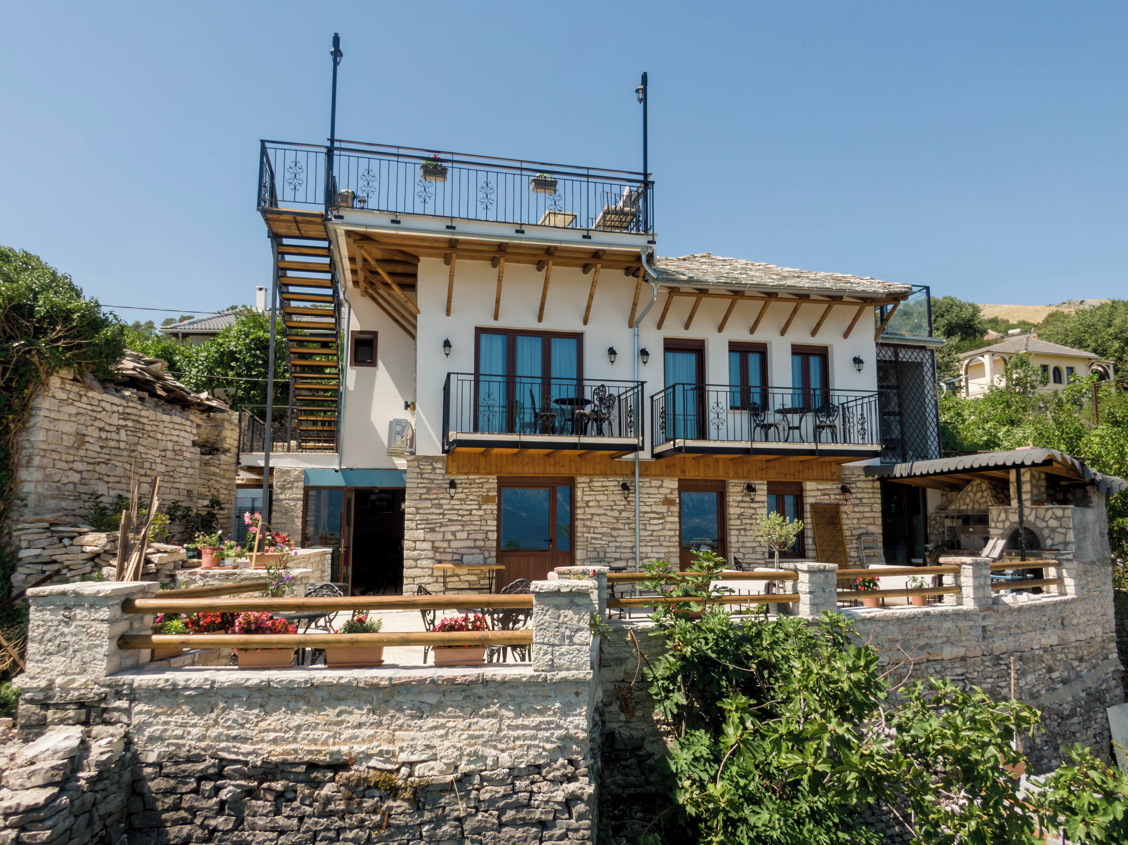 Un edificio de dos pisos con paredes de piedra, balcones con mobiliario exterior y una escalera de piedra.