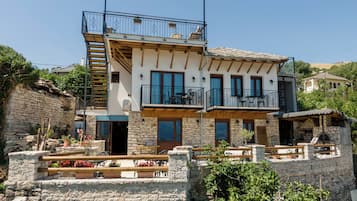 Un edificio de dos pisos con paredes de piedra, balcones con mobiliario exterior y una escalera de piedra.