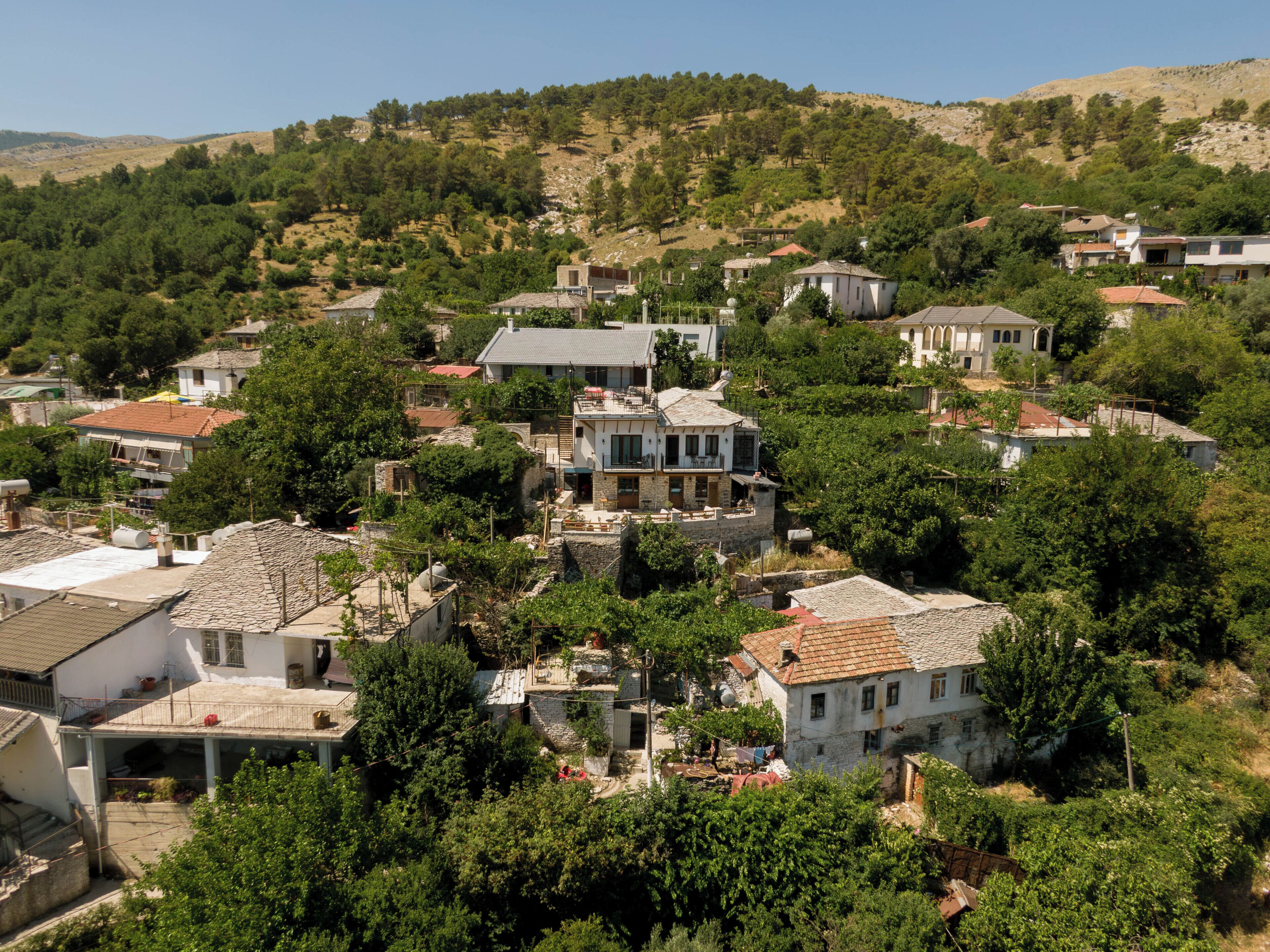 Un borgo collinare con case in pietra tradizionale, alcune con tetti piatti e altre a falde, immerso nel verde.