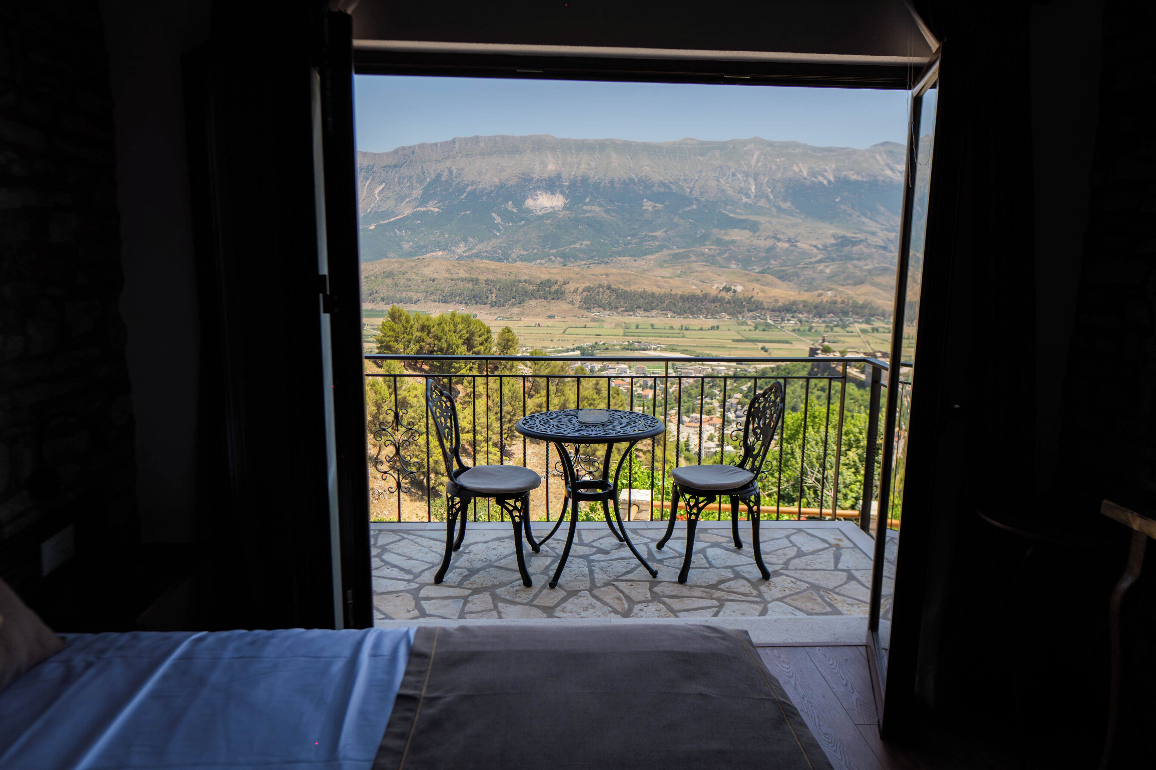A balcony with a table and chairs, overlooking a mountainous landscape.