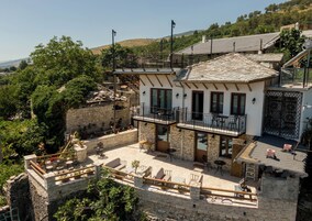 A building with a stone facade, a balcony with outdoor seating, and a view of the surrounding landscape.