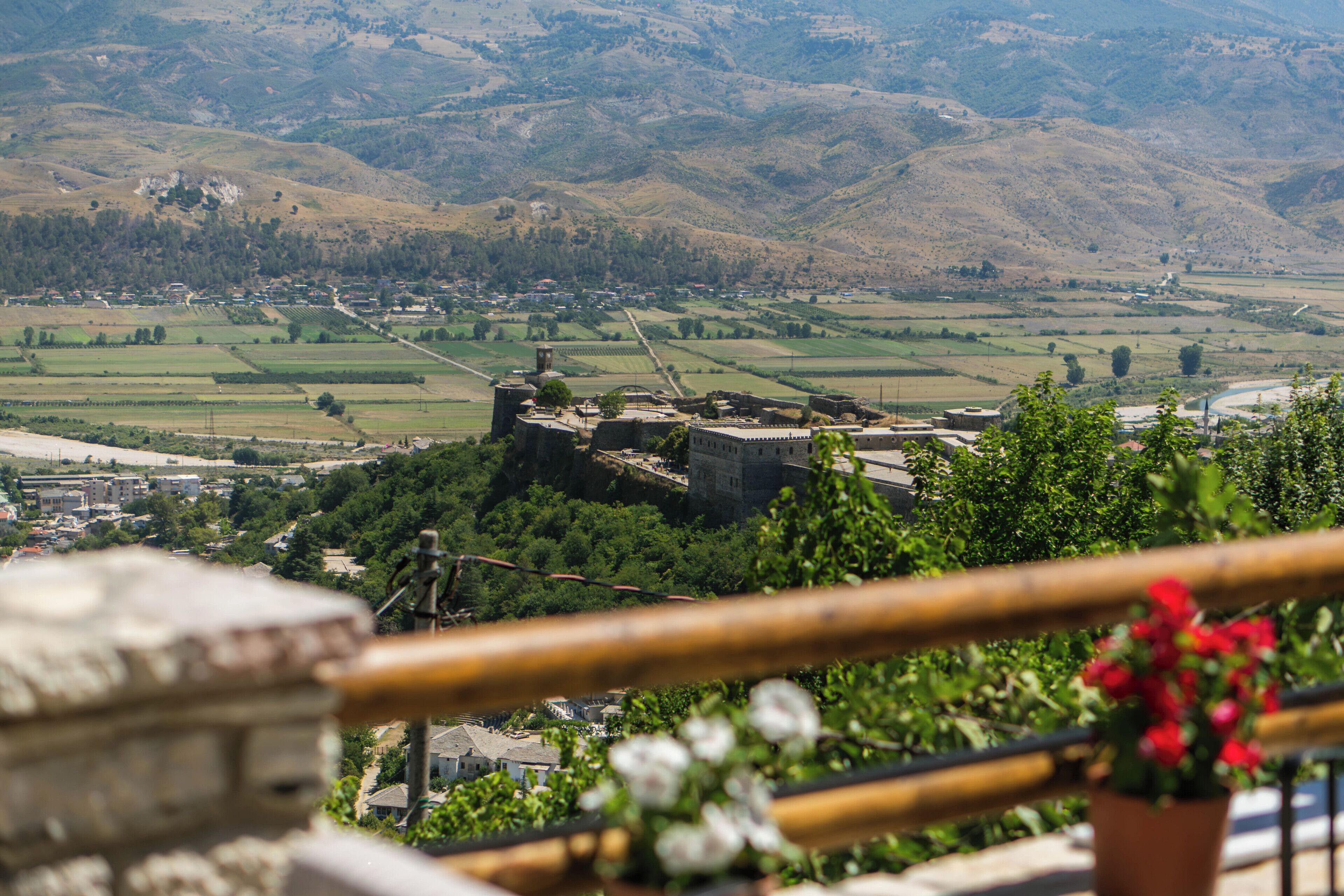 Vista panorámica de un castillo histórico sobre un valle con campos y un pequeño pueblo.
