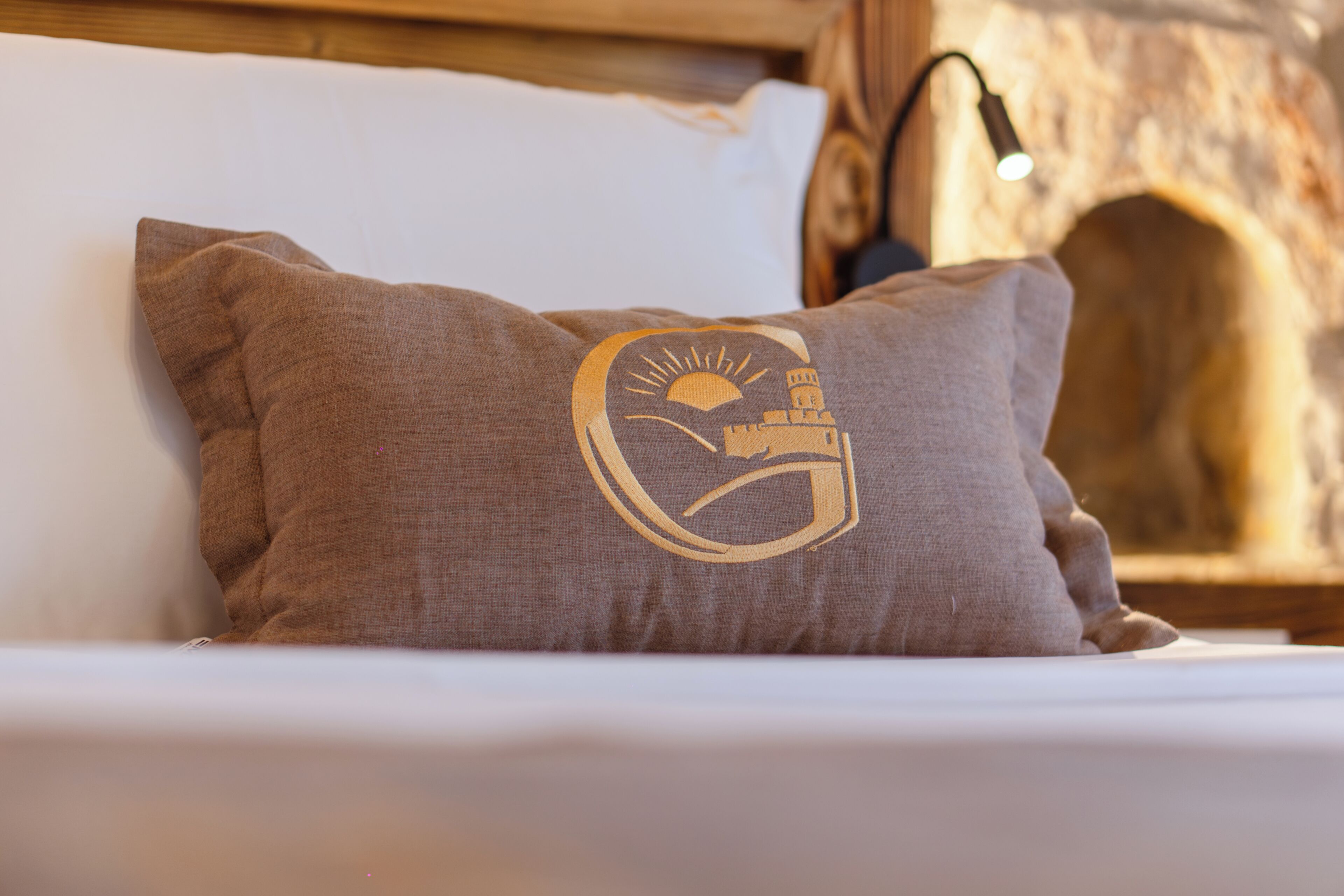 Ein Kissen mit Logo, ein Bett und eine Steinwand.