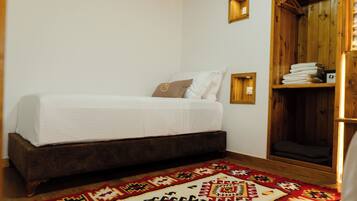 A room with a bed, a wooden wardrobe, a patterned rug, and a wall-mounted light fixture.