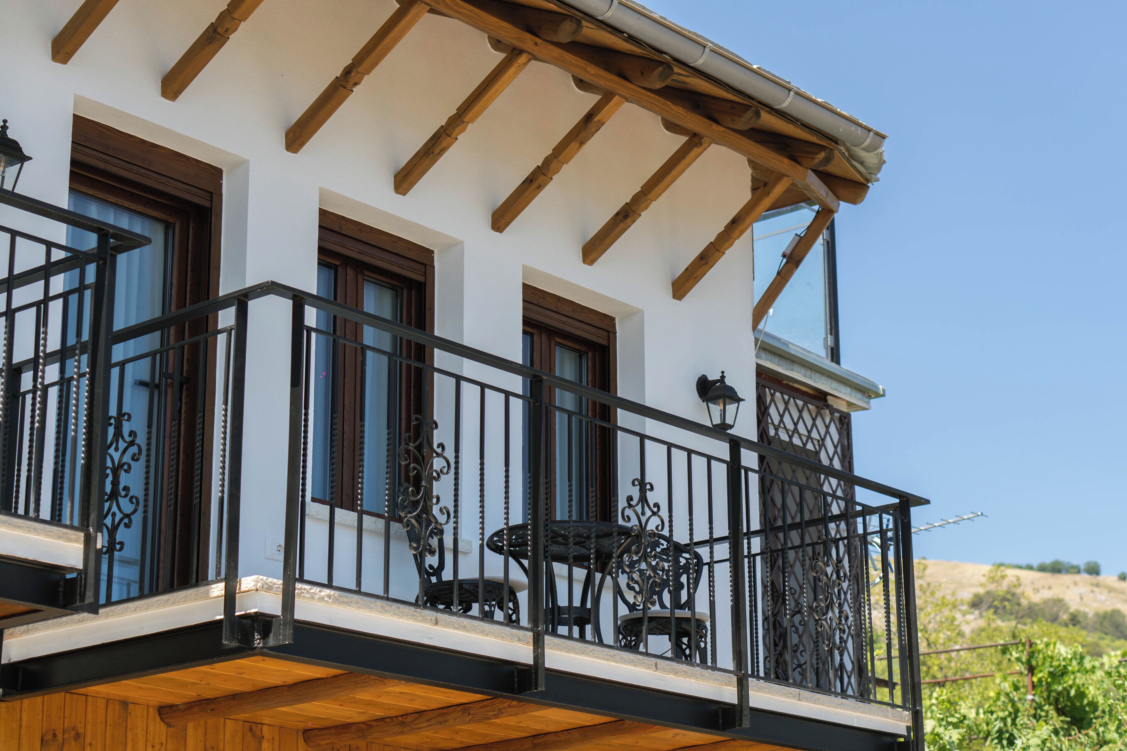 A two-story building with a balcony featuring a wooden floor, metal railing, and a table with chairs.