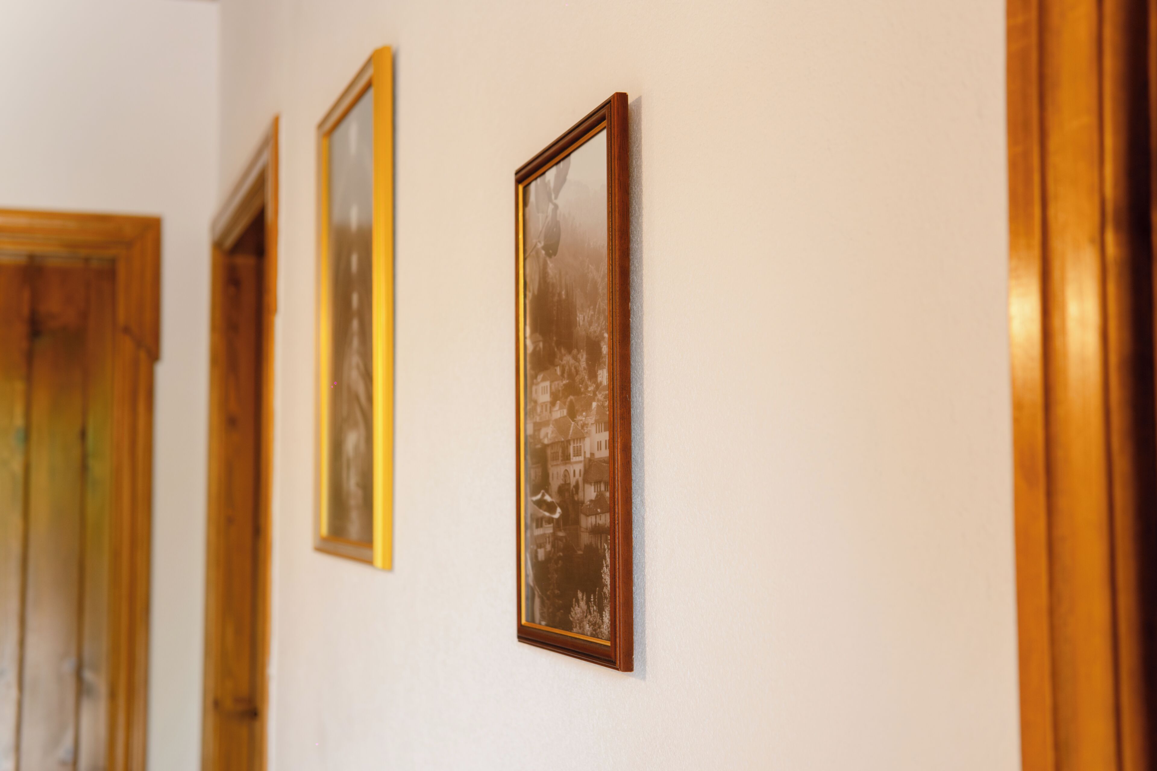 A hallway with framed pictures on the wall and wooden doors.