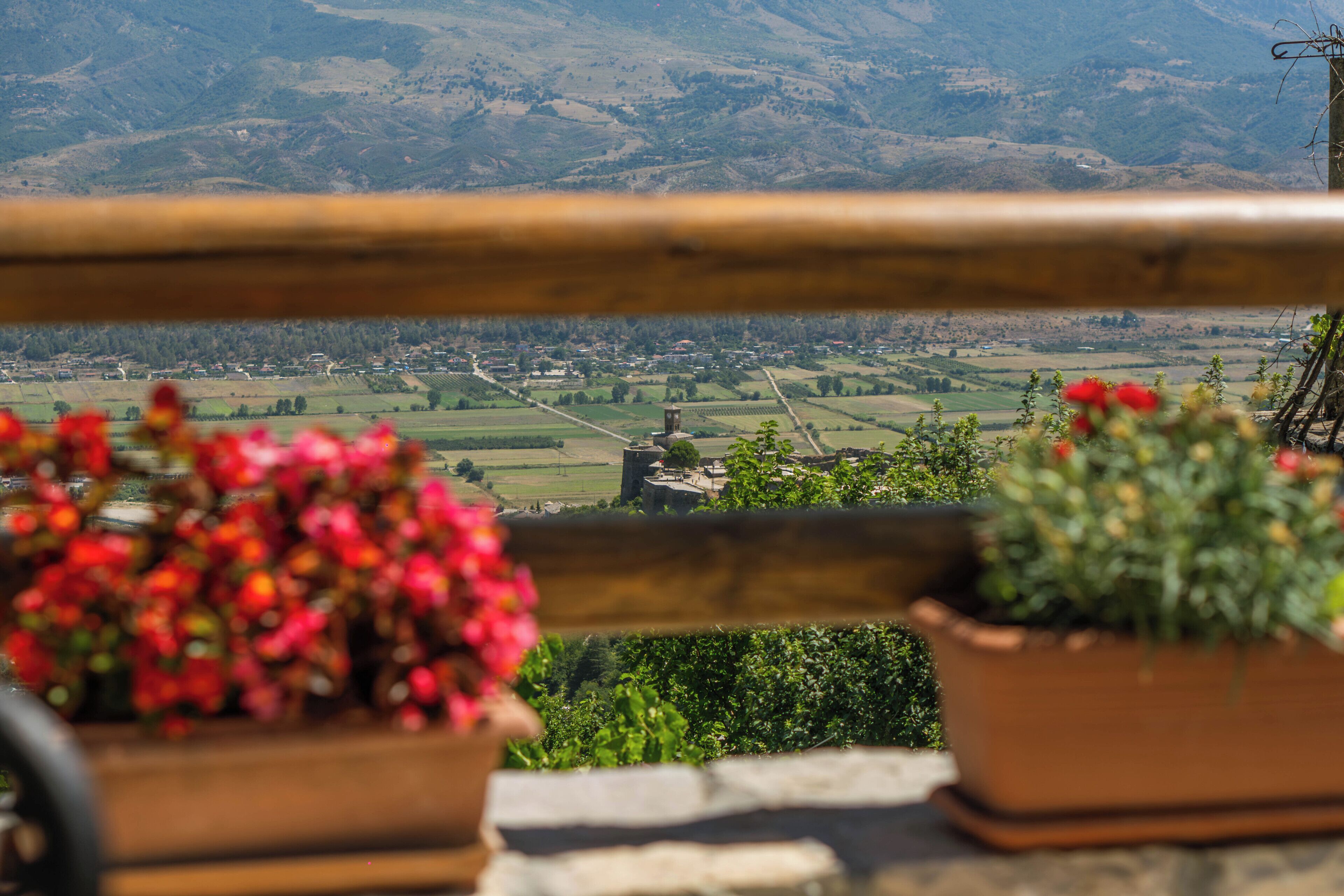 A balcony with a view of a rural landscape, including fields and a distant village.