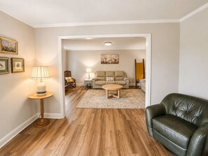 A living room with a wooden floor, a green leather sofa, a beige sofa, a coffee table, a lamp, and framed pictures on the wall. - Family friendly spacious 4 bed 3 BA house in West Asheville (Candler)
