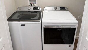 Deux machines à laver Maytag à chargement frontal, dans une buanderie avec un mur blanc et une prise de courant.