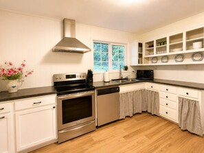 Een keuken met witte kasten, roestvrijstalen apparatuur, een raam met uitzicht op groen en een afwasservice met borden.