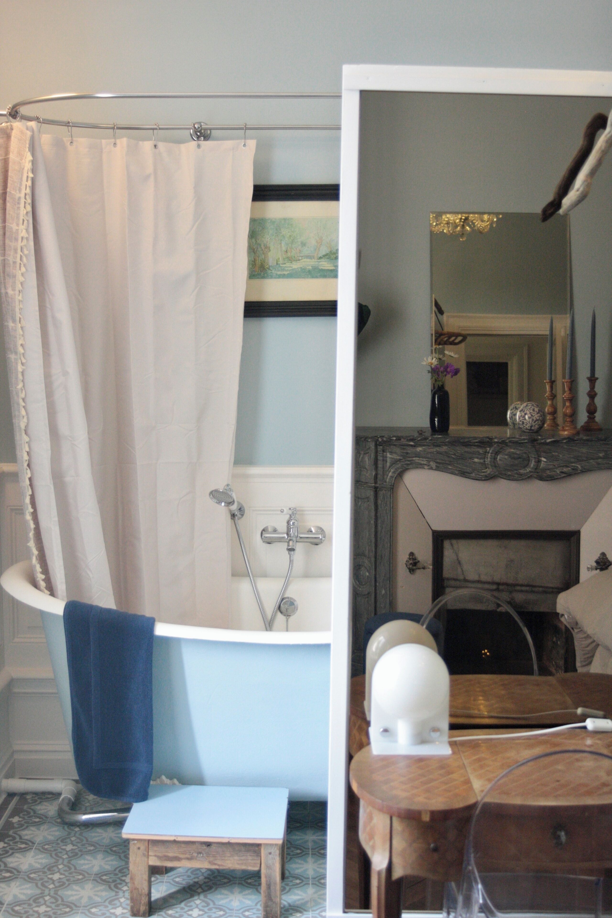 A bathroom with a bathtub, a small wooden stool, and a mirror reflecting a fireplace.