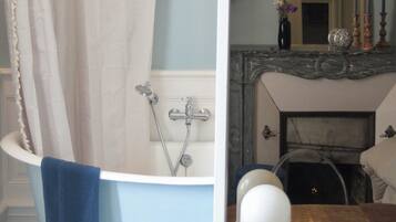 A bathroom with a bathtub, a small wooden stool, and a mirror reflecting a fireplace.