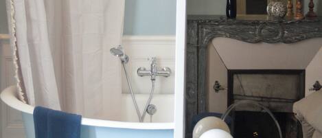 A bathroom with a bathtub, a small wooden stool, and a mirror reflecting a fireplace.
