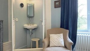 A room with a round armchair, a small stool, a white sink, and a window with a view.