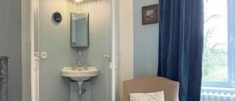 A room with a round armchair, a small stool, a white sink, and a window with a view.