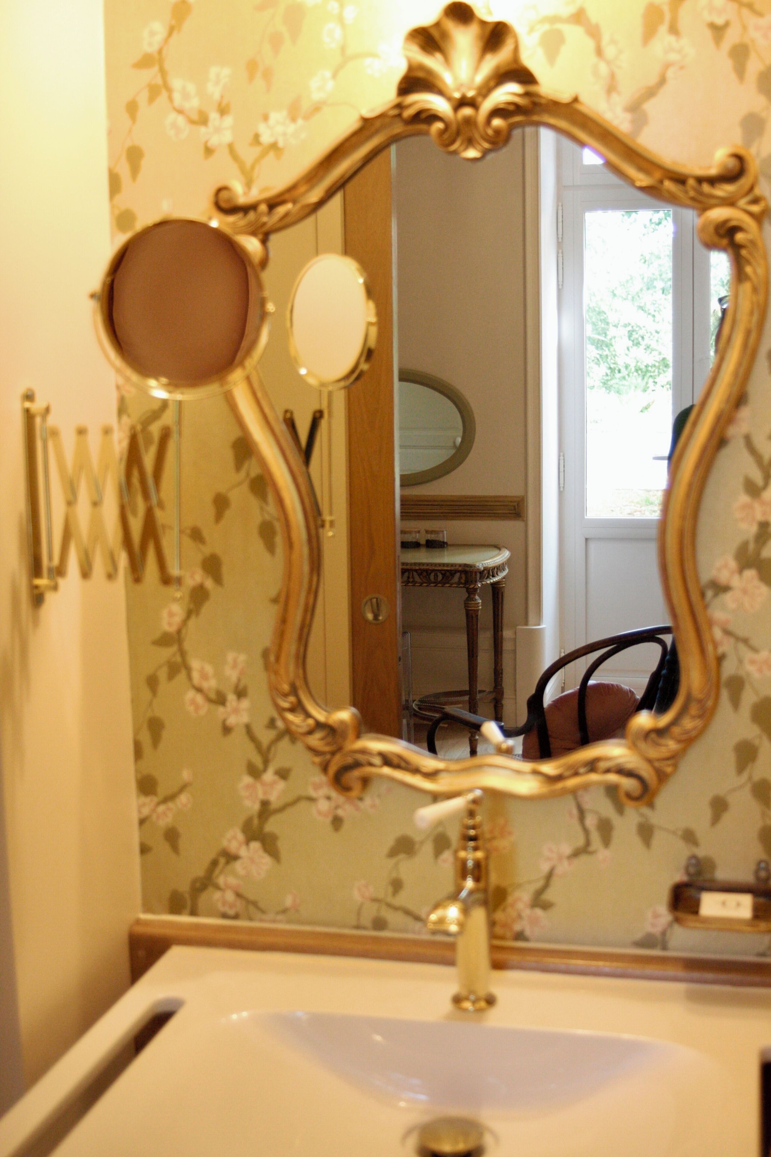 Un baño con lavamanos, espejo y papel tapiz con motivos florales.