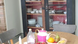 A dining table set with plates, cups, a teapot, a bottle, and a fruit basket.