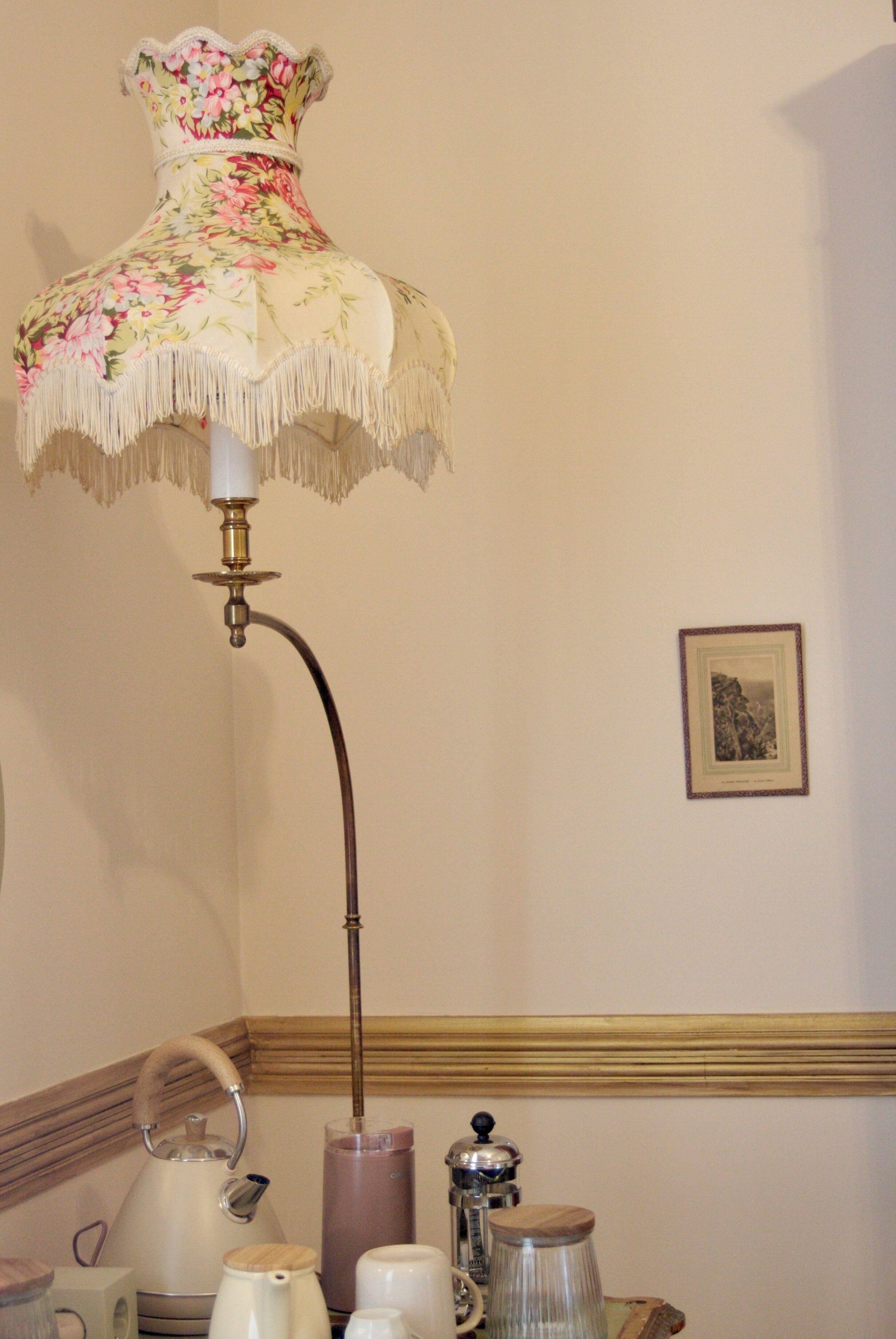 A room with a floral lamp, a framed picture on the wall, and various kitchen appliances.
