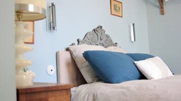 Quarto com cama, mesa de cabeceira, luminária na parede e quadro emoldurado.