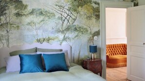 A bedroom with a bed, a nightstand, a lamp, and a door leading to another room.