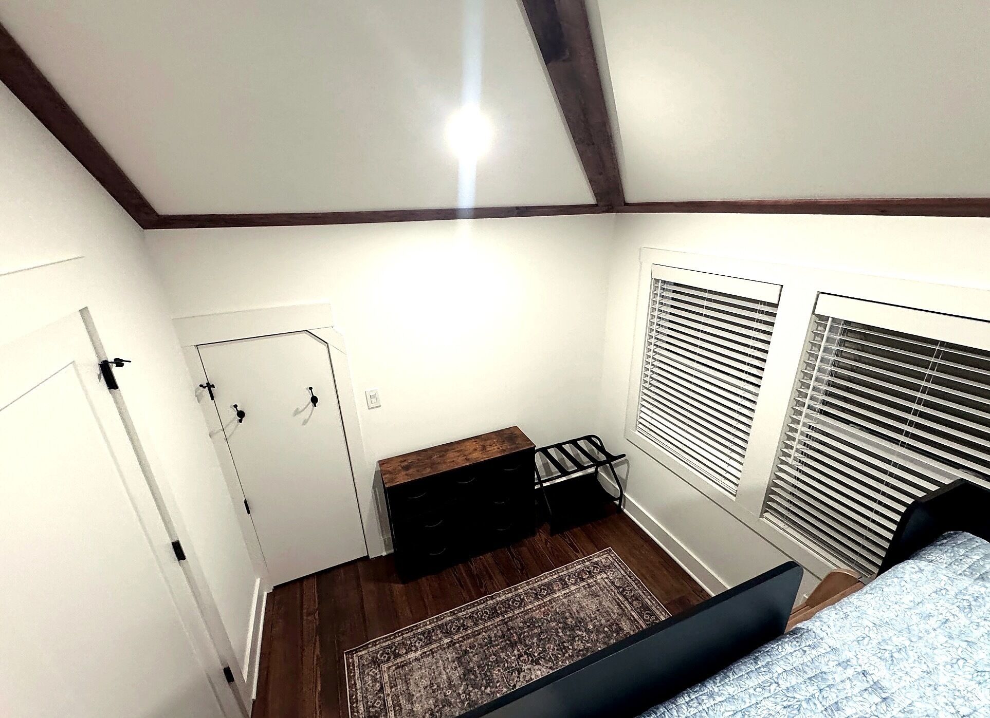 A room with a door, a small bench, a window with blinds, and a patterned rug.