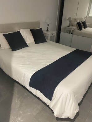 A neatly made bed with white and dark blue bedding, a bedside table with a lamp, and a mirror on the wall. - Spacious 3-bedroom Villa in marvelous Cap-d'Ail with AC (Cap-d'Ail)
