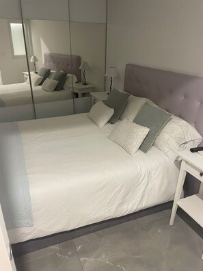 Ein ordentlich bezogenes Bett mit Kissen, ein Nachttisch mit Lampe und ein Spiegel an der Wand.