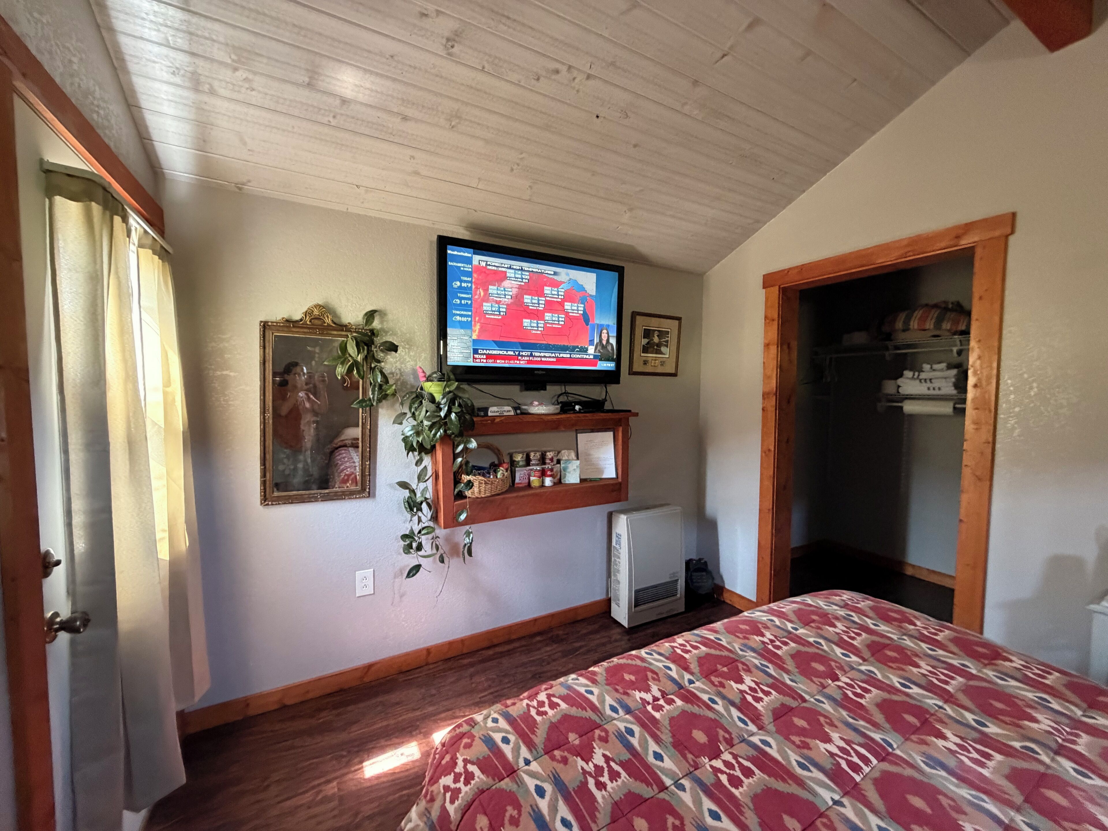 Une chambre avec un lit, un téléviseur fixé au mur, un petit réfrigérateur et une porte en bois.