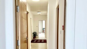 Un couloir avec une porte en bois sur la gauche, une plante en pot et un tapis rouge à motifs sur le sol.