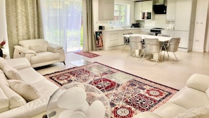 Un salon moderne avec un canapé, un coin repas avec des chaises, une cuisine équipée de meubles et une grande fenêtre.