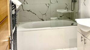 Une salle de bain moderne avec un mur en marbre, une douche en verre, une baignoire et un lavabo blanc.