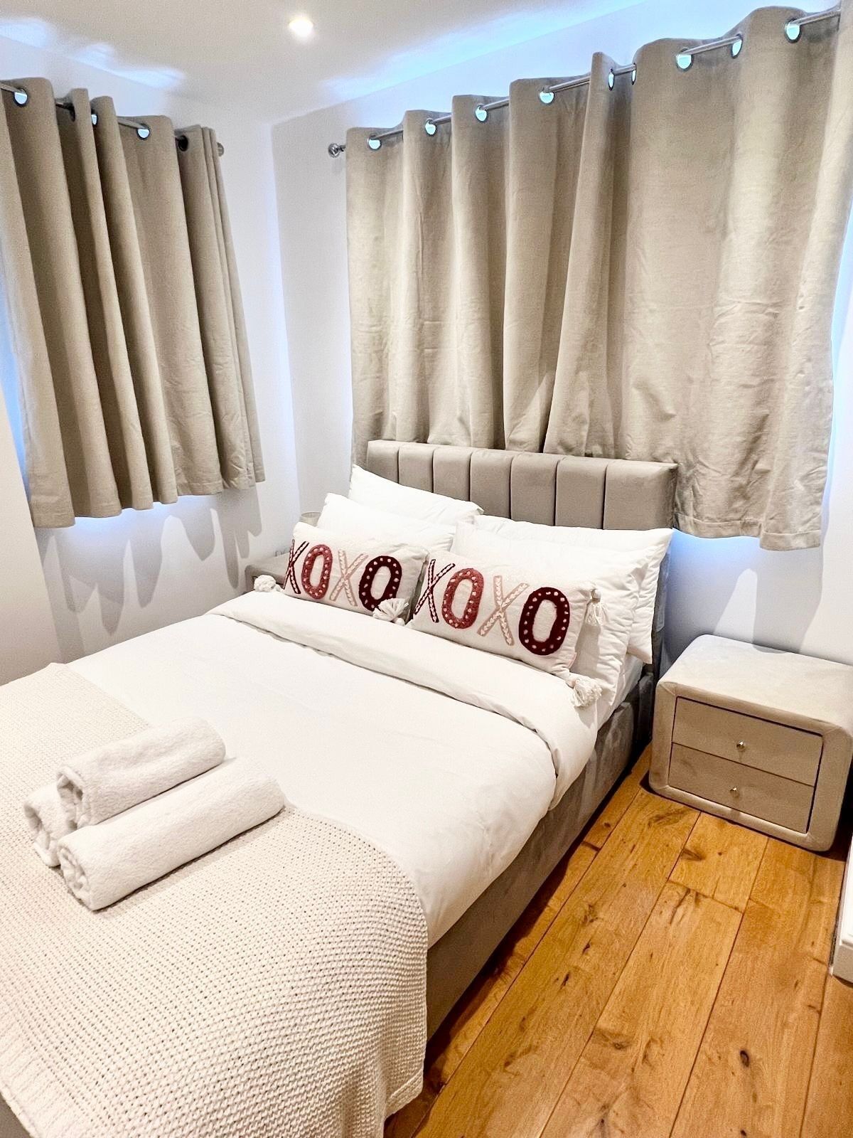 Un lit bien fait, avec une couette blanche et des oreillers, un plancher en bois et une table de chevet dotée d’un tiroir.