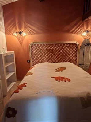 A bedroom with a white bed, a headboard with a diamond pattern, and a wall-mounted light fixture. - The Irises of Mapaly - SALERNES (SALERNES)