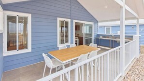 A blue house with a covered patio, white railings, and a wooden table with chairs.