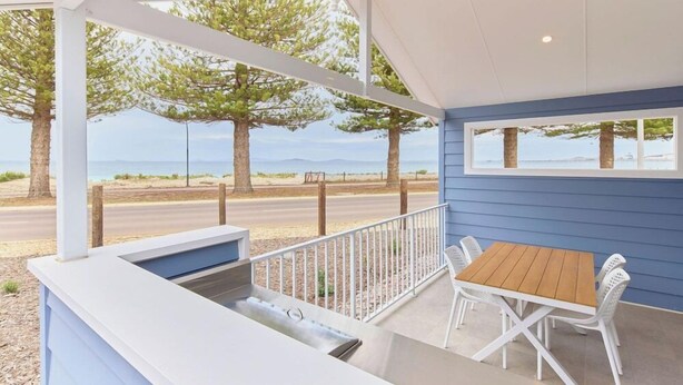 A covered outdoor seating area with a table and chairs, overlooking a road and trees.
