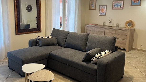 A living room with a sectional sofa, a small round table, a ceiling fan, and a dresser with decorative items. - 500 meters from the beach, a 3-bedroom family home with a terrace and barbecue (Agde)